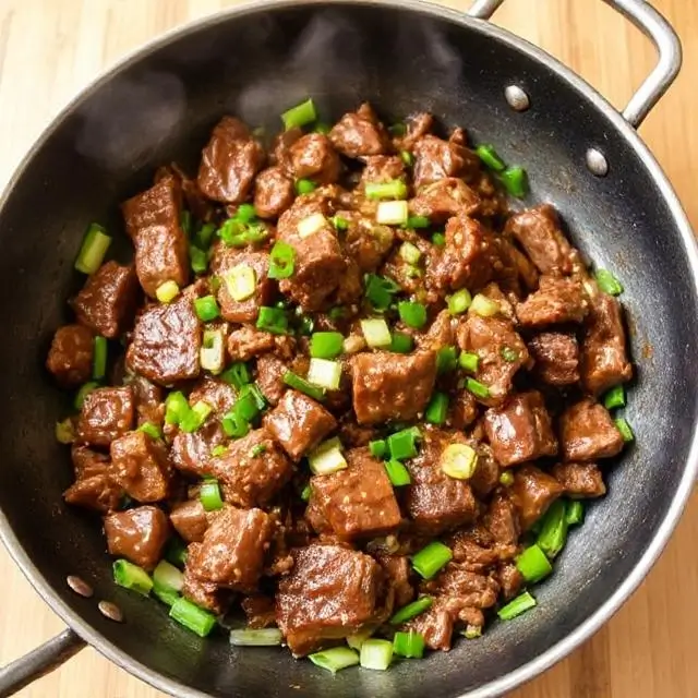 Sizzling Mongolian Beef with scallions in a wok.